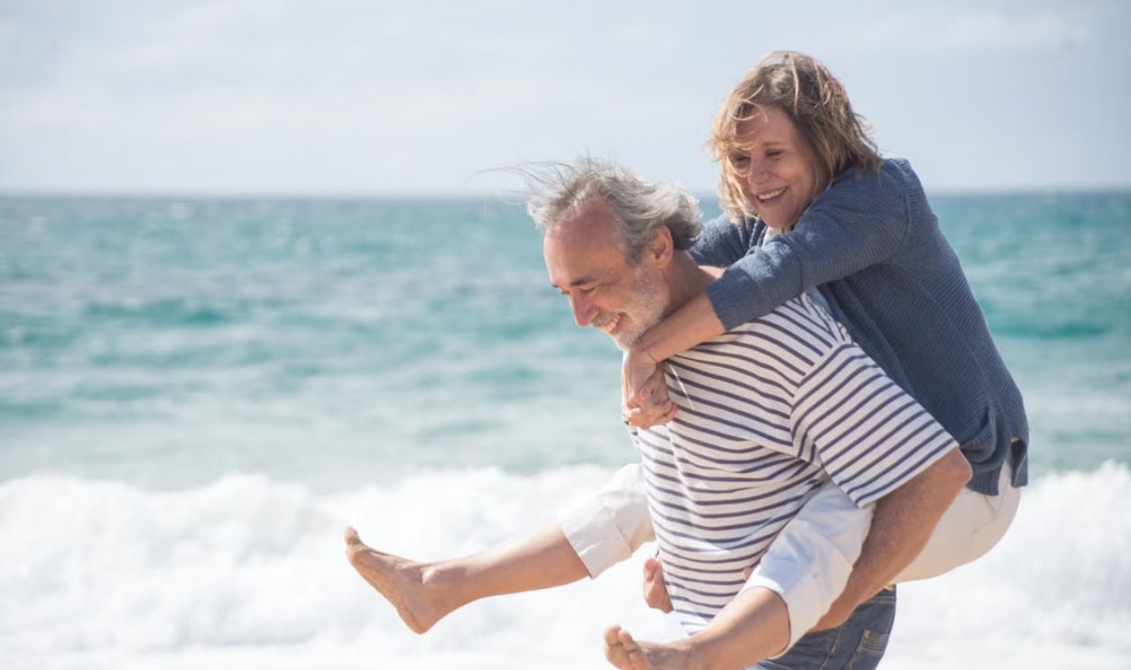 Happy senior couple on a beach in Portugal, sharing a joyful moment by the ocean.
