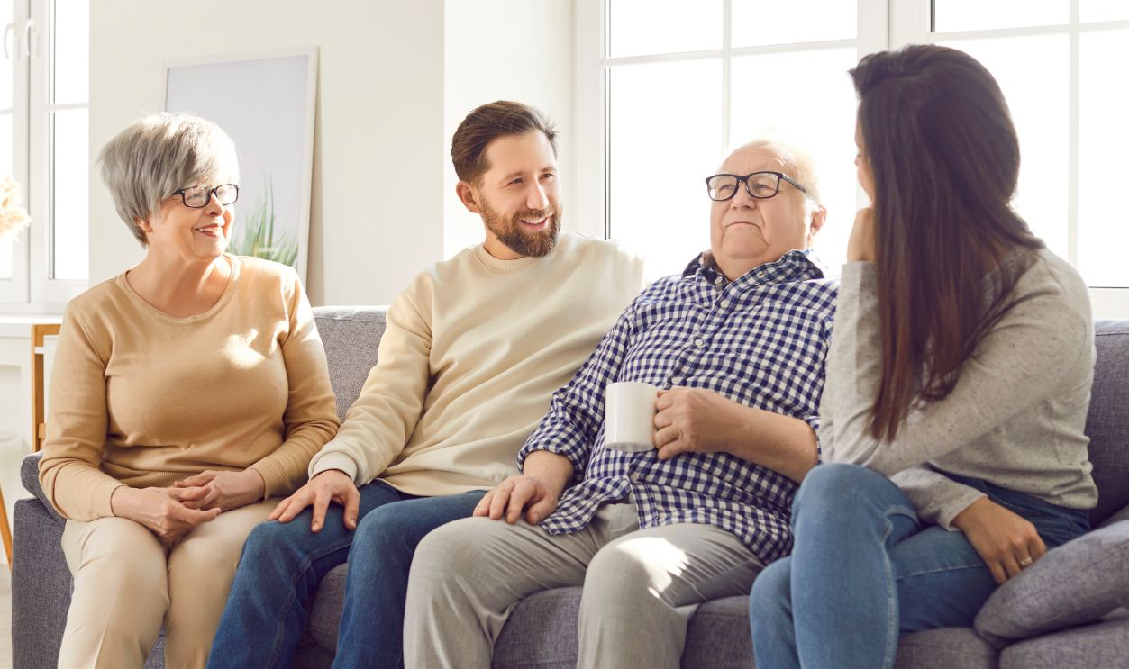 Portrait of happy joyful smiling family of senior old parents and their adult children man and woman sitting on sofa in living room at home, talking with cup of tea. Family leisure concept.