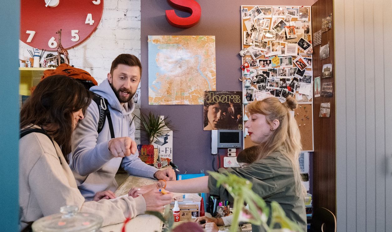 Guests checking in at a hostel reception with a warm interaction between a couple and staff.