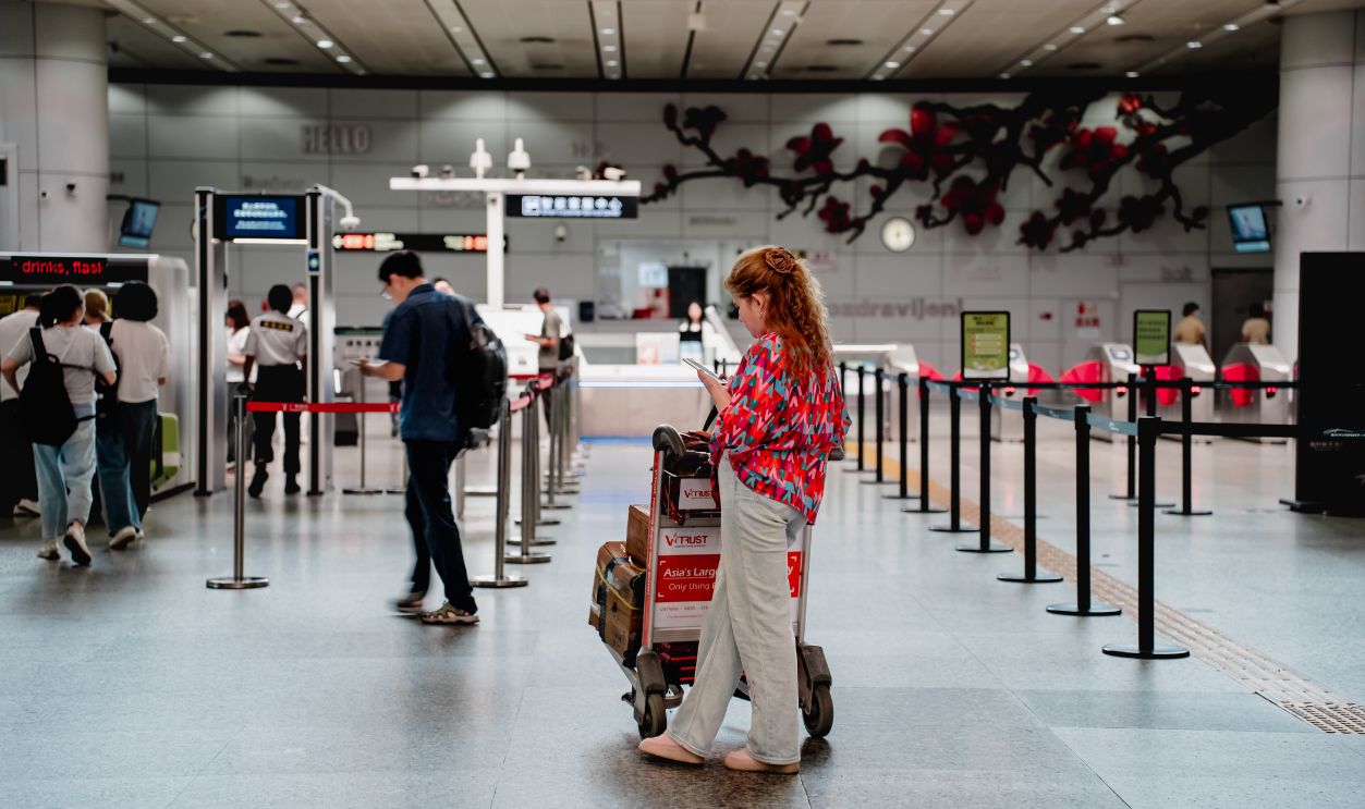 A traveler checks her phone while waiting with a luggage cart at a busy airport terminal in Guangzhou.