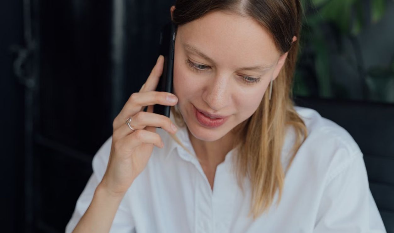 A professional woman in a white shirt making a phone call in an indoor setting, showing communication and business engagement.