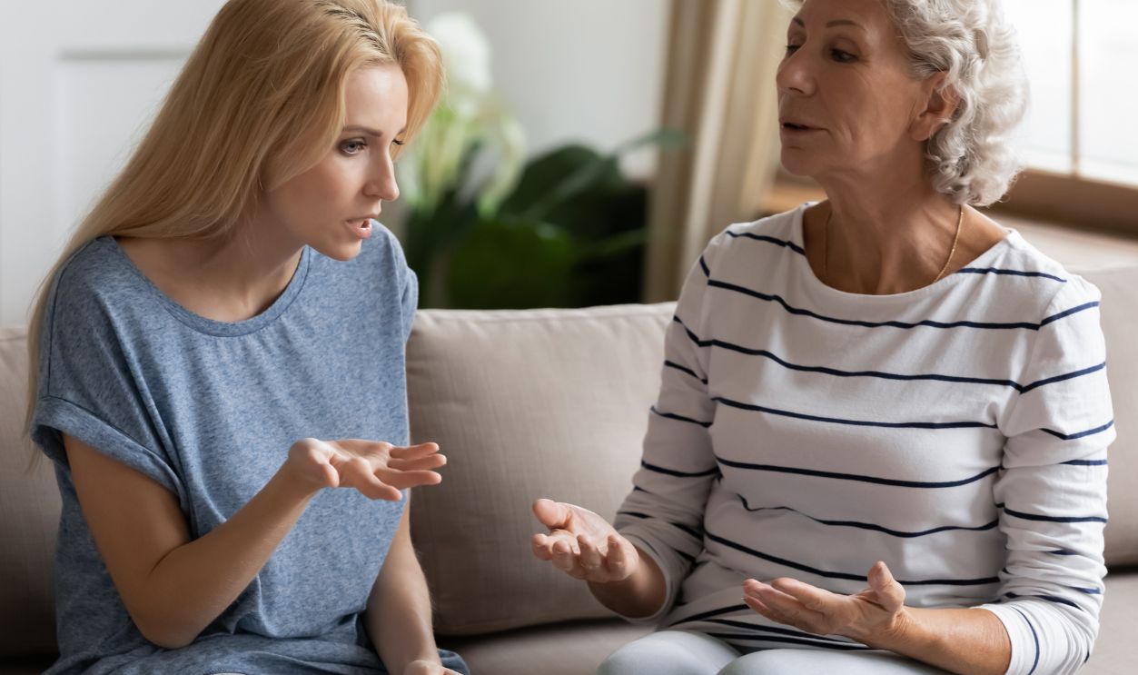 Stressed young blonde grown up daughter arguing with nervous old mature mother, sitting together at home. Irritated elderly woman lecturing adult child, different generations misunderstanding gap.