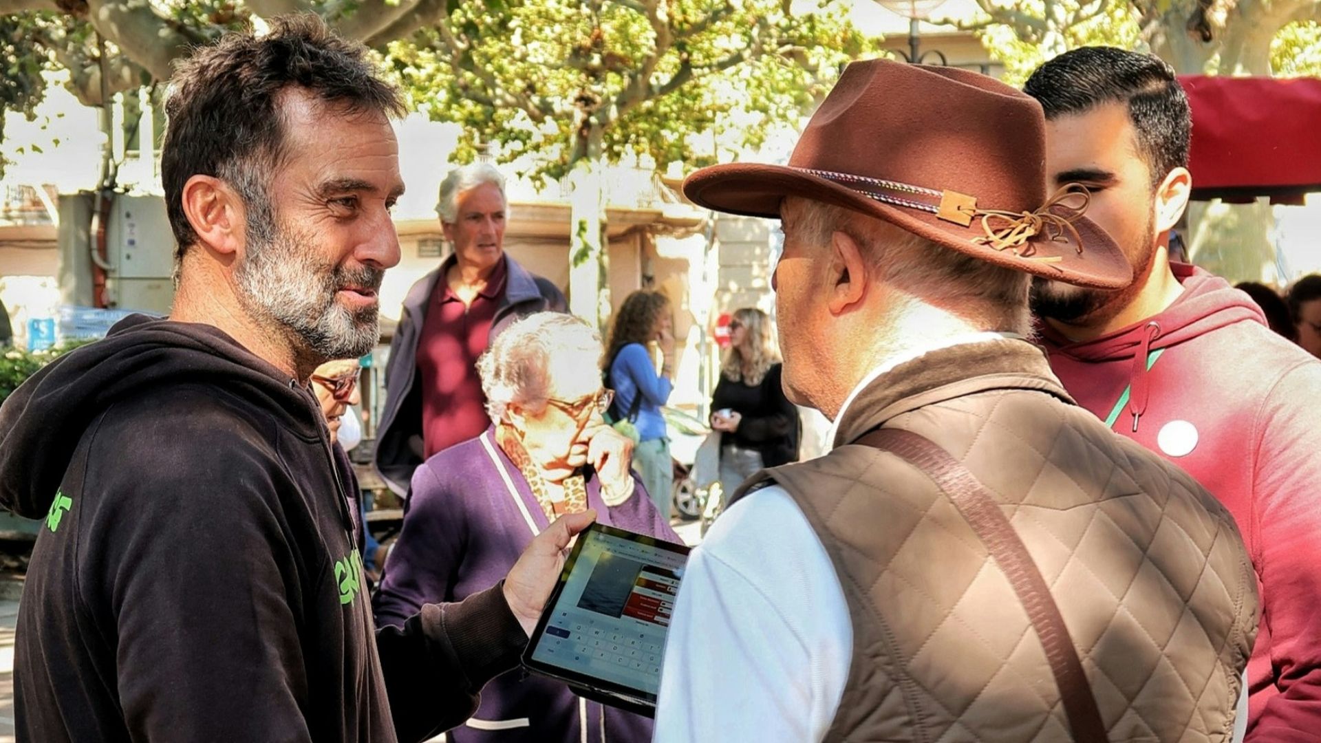 Men gathered outdoors, one holding a tablet