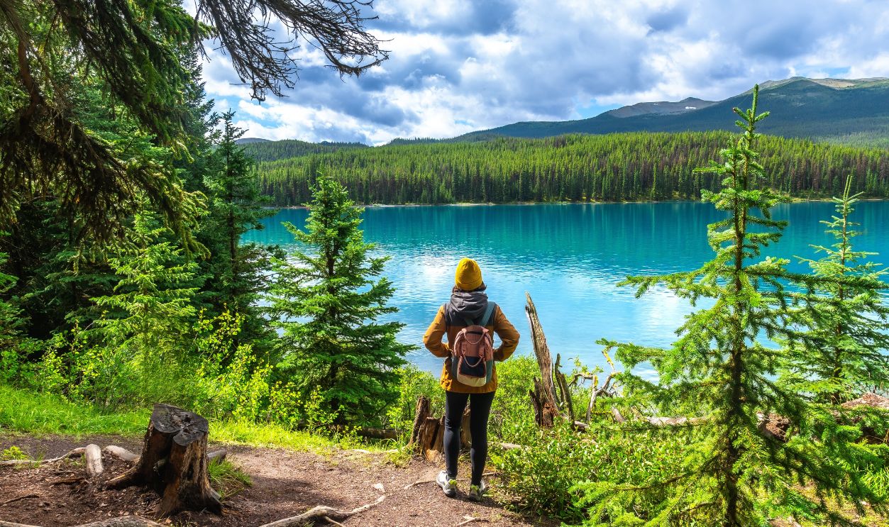Female hiker with a backpack admiring the stunning turquoise waters of maligne lake, surrounded by lush evergreens and majestic mountains in jasper national park