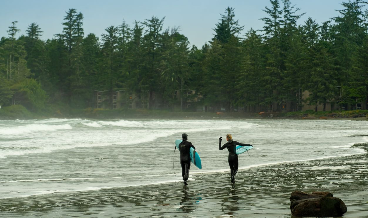 Tofino, British Columbia, Canada - November 05, 2021 - Surfers walking on the beach of Cox Bay, a popular surf spot in Tofino Vancouver Island Canada