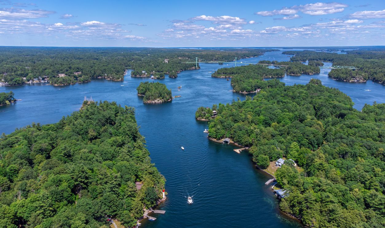 Scenic aerial view of the Thousand Islands region on the Saint Lawrence River, featuring lush islands, boats, cottages, and the Thousand Islands International Bridge, Ontario, Canada (July 2021)