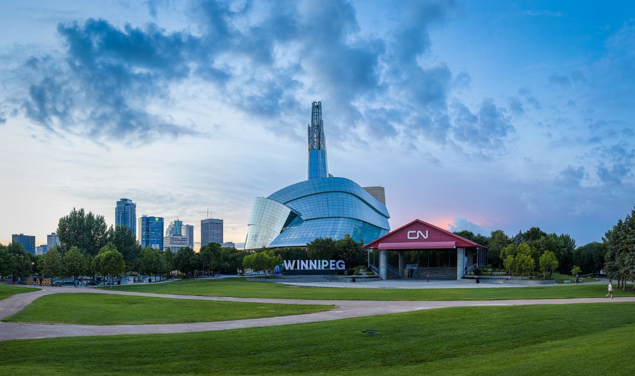 Winnipeg, MB, Canada - September 2022: The Canadian Museum for Human Rights and the Winnipeg Sign at the Forks with downtown buildings and a cloudy blue sky in the background