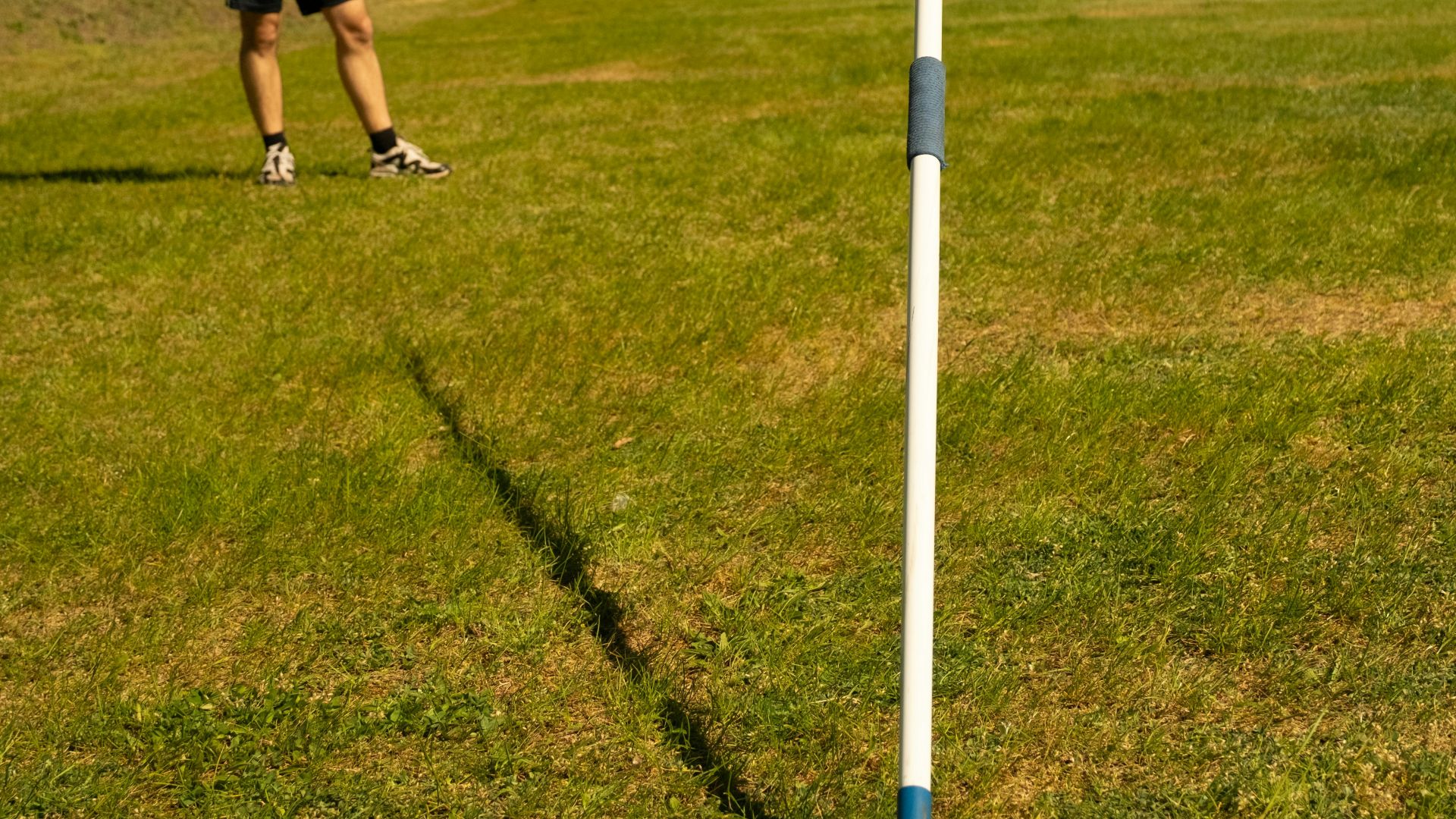 Person standing on a grassy field with a striped pole
