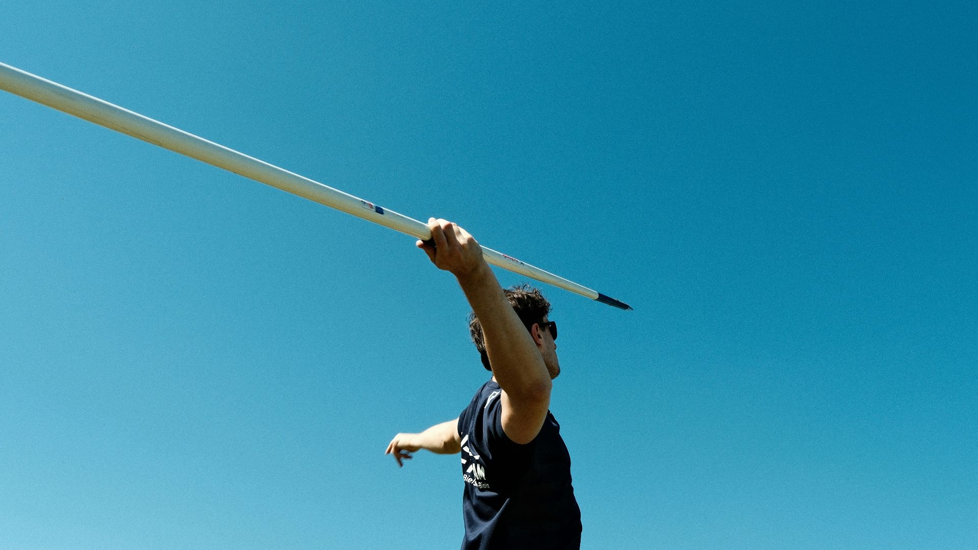 Athlete holding a javelin against a clear blue sky