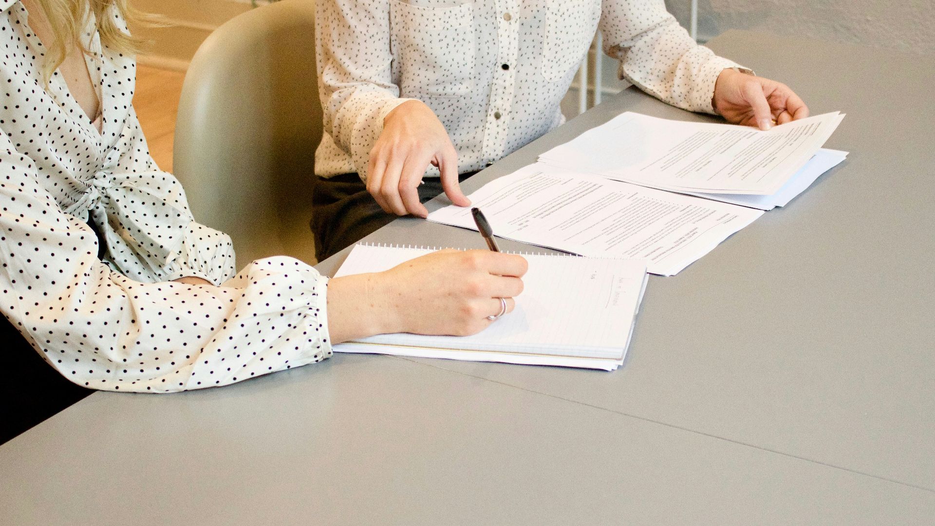 woman signing on white printer paper beside woman about to touch the documents