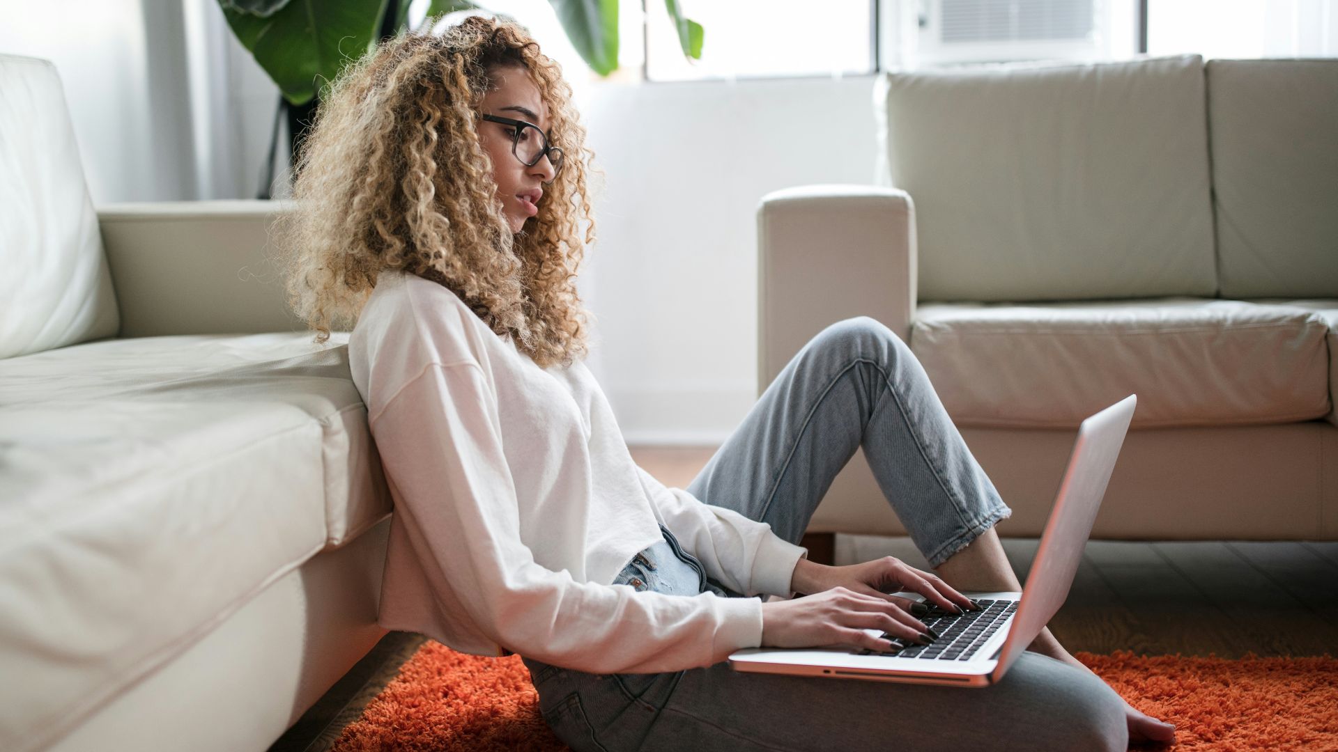 woman sitting on floor and leaning on couch using laptop