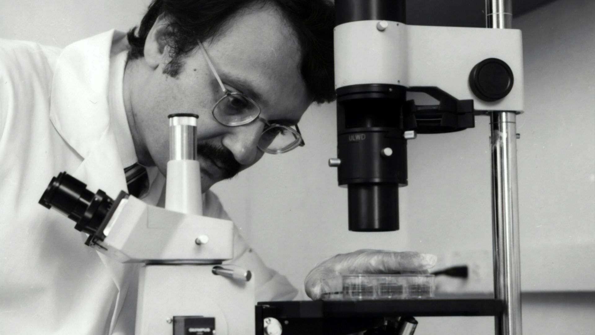 grayscale photography of doctor using microscope