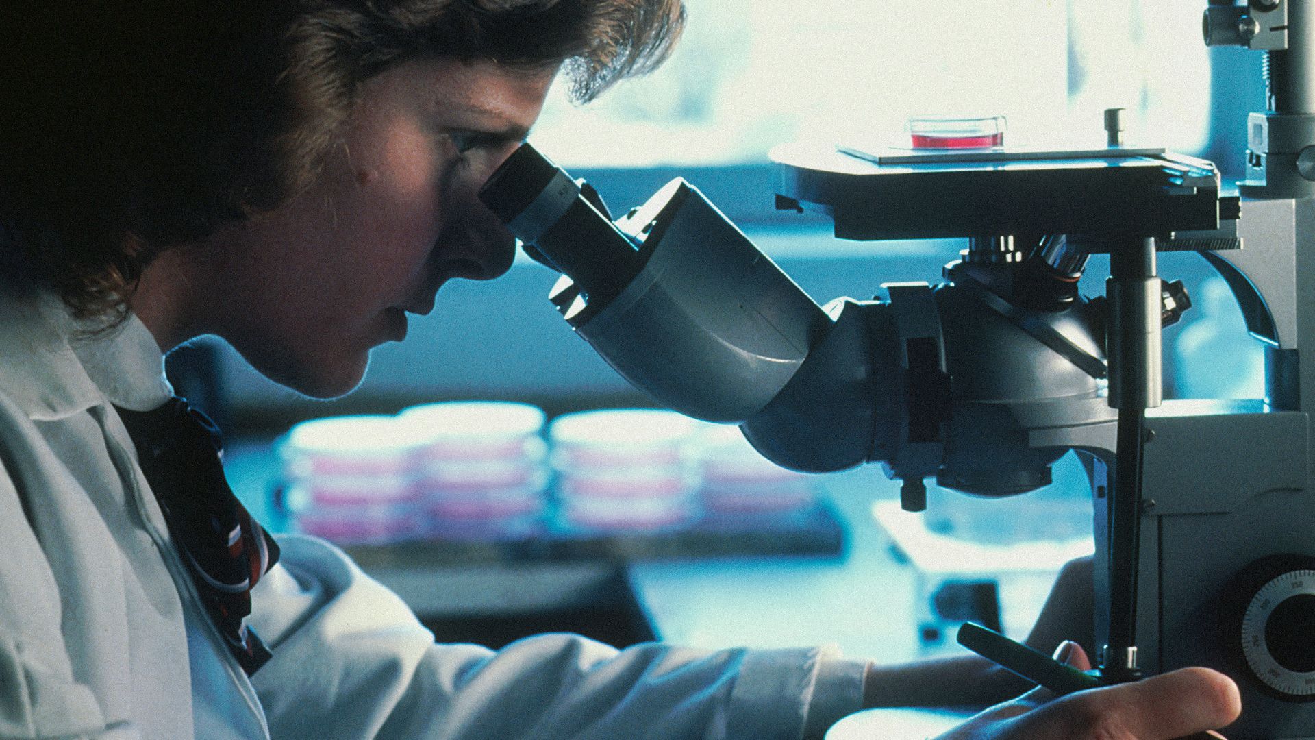 A person in a white lab coat looking through a microscope in a laboratory