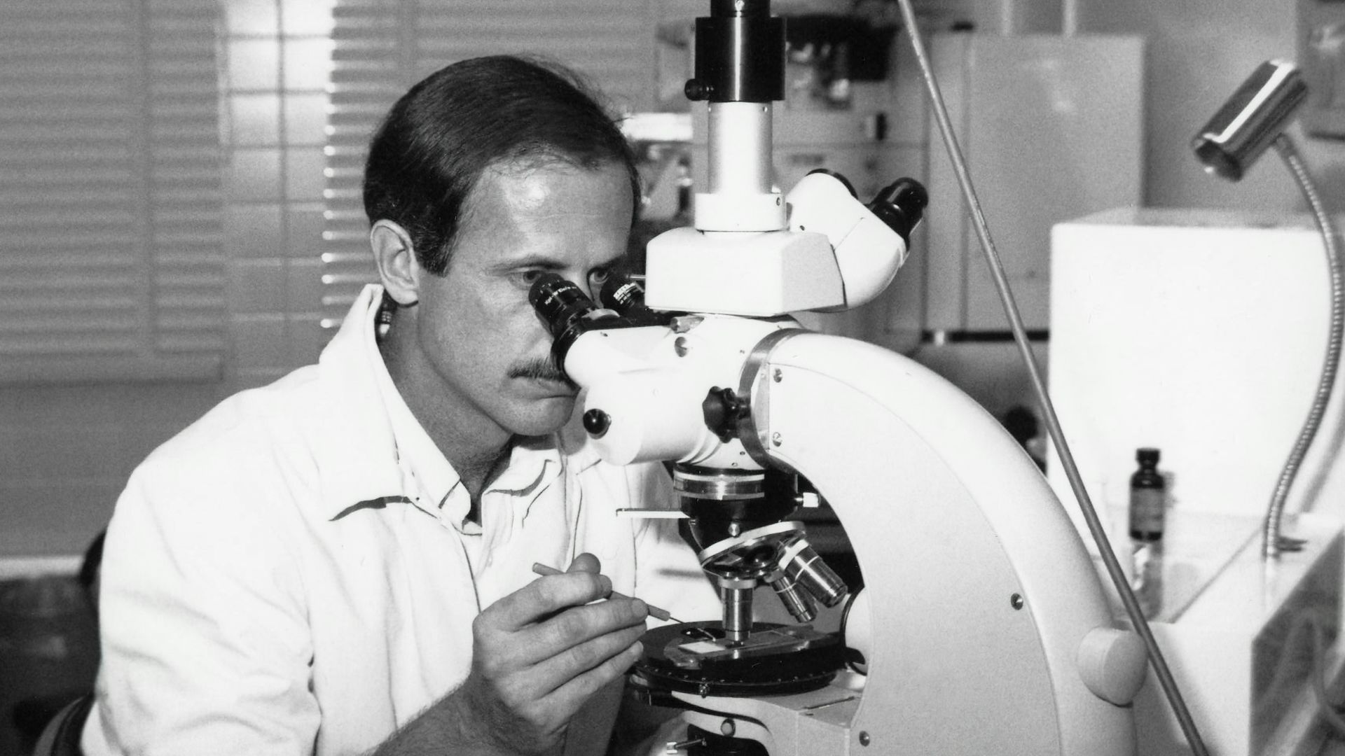 a black and white photo of a man looking through a microscope