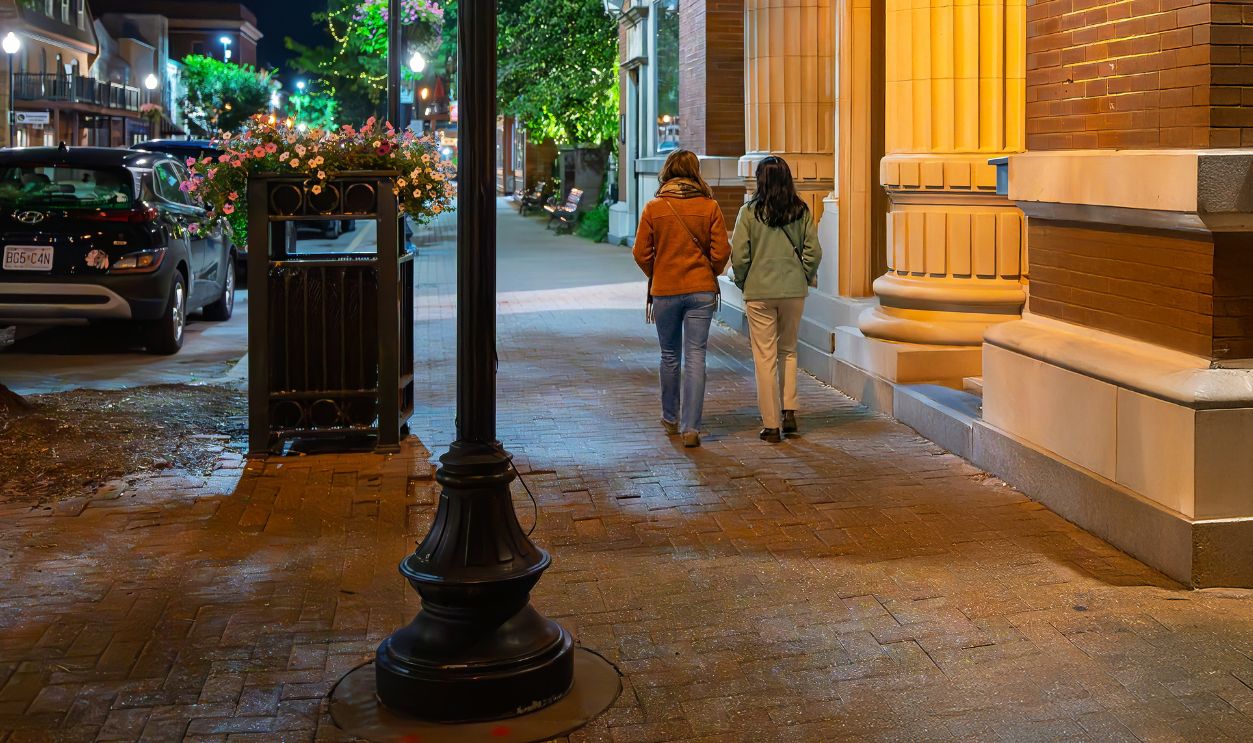 St. Charles, Missouri - July 21 2025: Two young women walk along the brick paved sidewalk at night in the historic downtown district of St. Charles, Missouri.