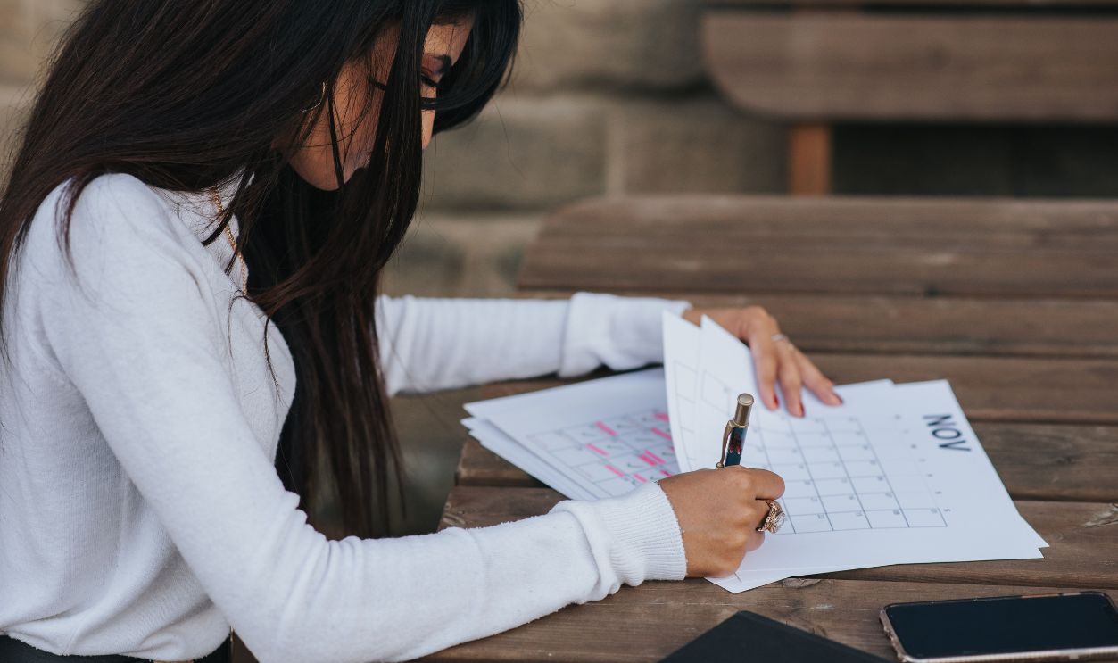 Young woman writing in a calendar while planning her schedule at an outdoor wooden table.