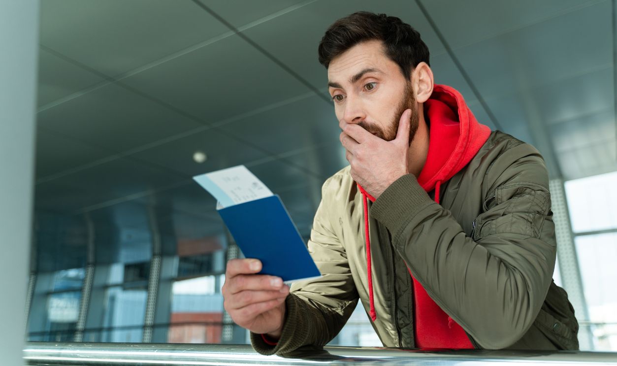 Waist up portrait of shocked man standing at the airport and looking at his passport with surprised expression while waiting for departure. Technologies and people concept