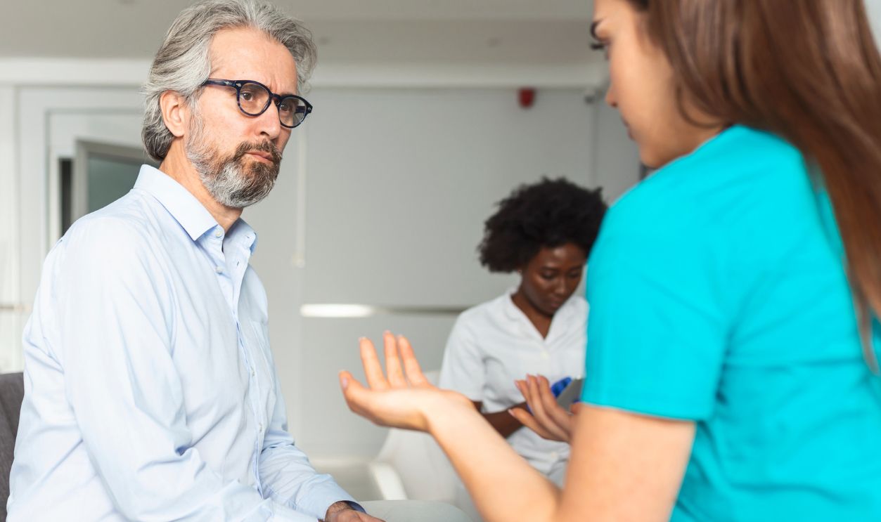 Young female doctor and senior man communicating in a waiting room at hospital. medicine, healthcare and people concept - doctor and patient meeting at hospital