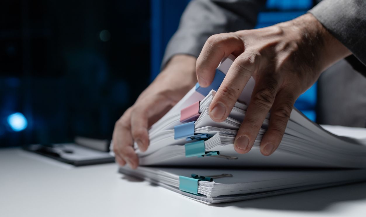 An employee held a large pile of documents in his hand, Large piles of work documents on desks are being sorted by employees, Important documents are stacked.