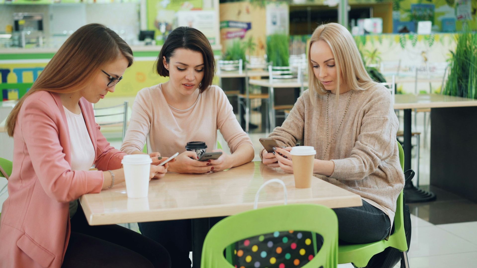 Three women looking at their phones at a cafe table