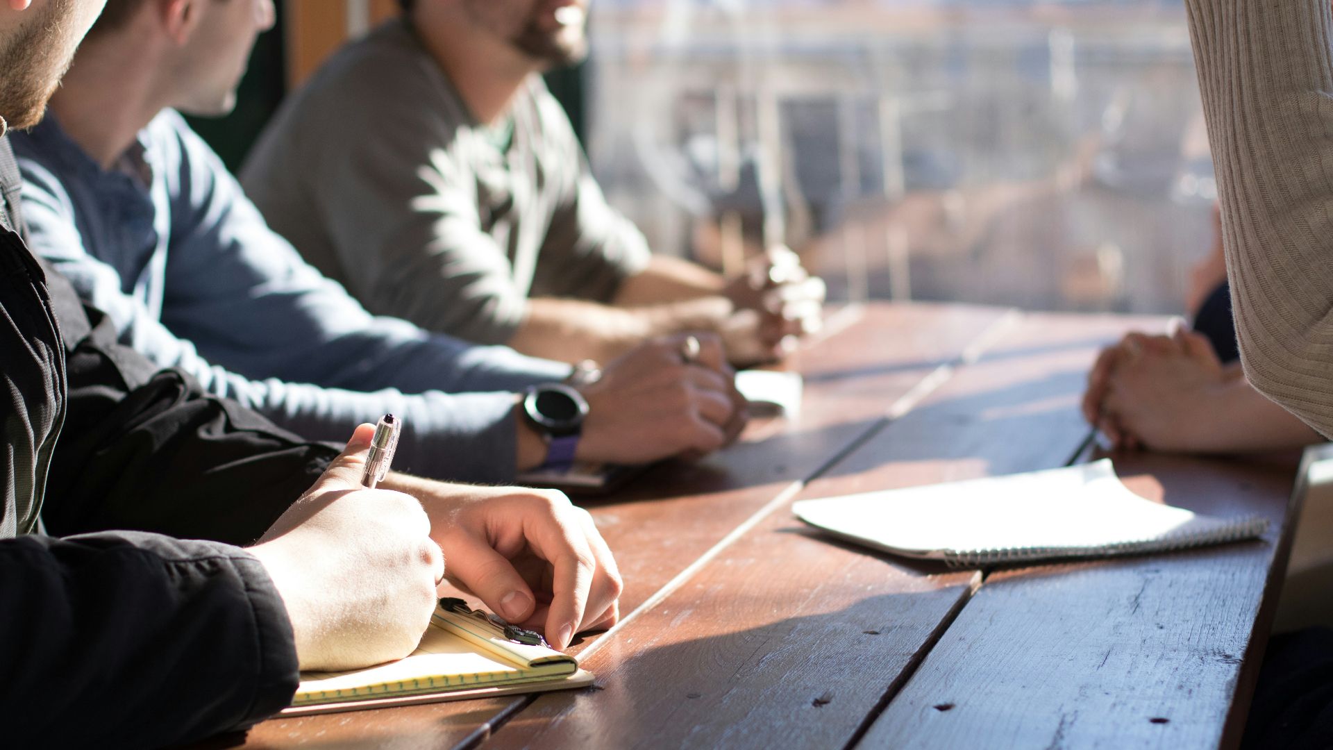people sitting on chair in front of table while holding pens during daytime