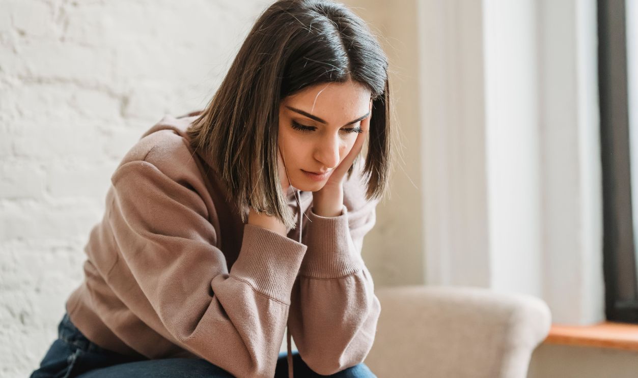 A young woman sits pensively on a sofa, conveying emotions of deep thought and contemplation indoors