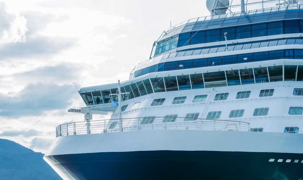 A large cruise ship in the water with mountains in the background