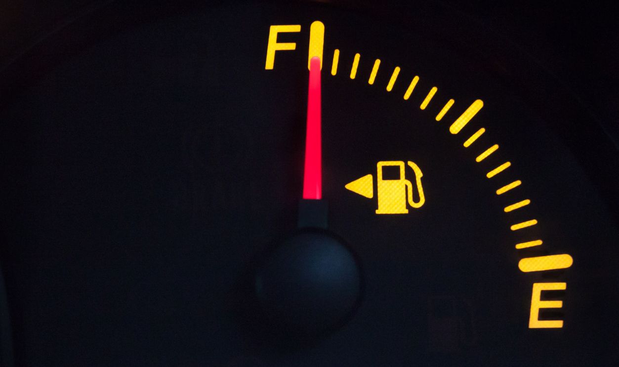Fuel gauge showing a full tank. Yellow glowing meter with a red needle. Isolated against black background.