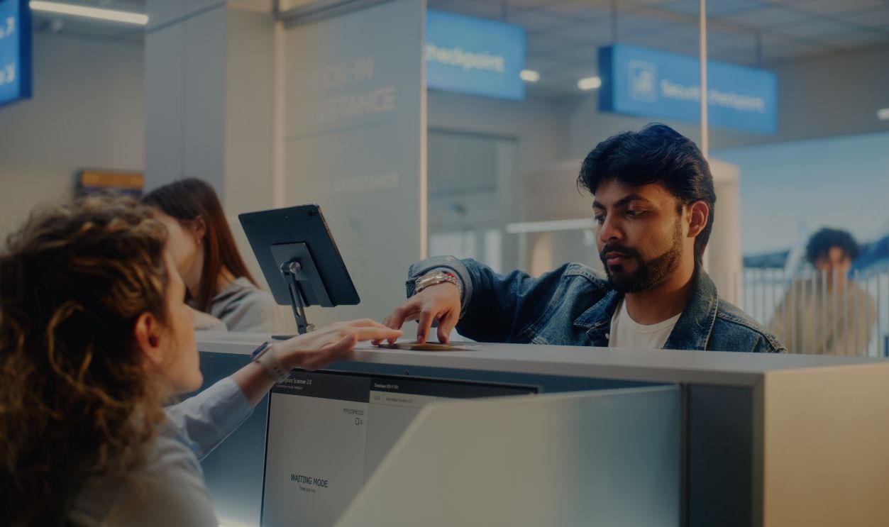 Shutterstock-2612531317, Airport Check-in Counter: Female Airline Worker Checking Personal ID Data of Passenger on Computer, Giving Documents and Boarding Pass to Indian Man. Passport Check in International Airport Terminal.