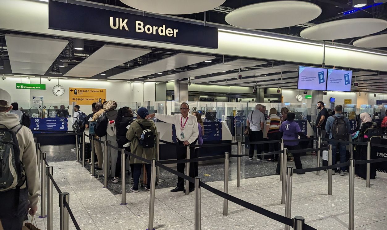 Passengers queue at the UK Border passport control area in London Heathrow Airport on June 18, 2025, in London, UK. Immigration officers and airport staff manage the arrivals flow as travelers wait behind security barriers in a modern terminal environment.