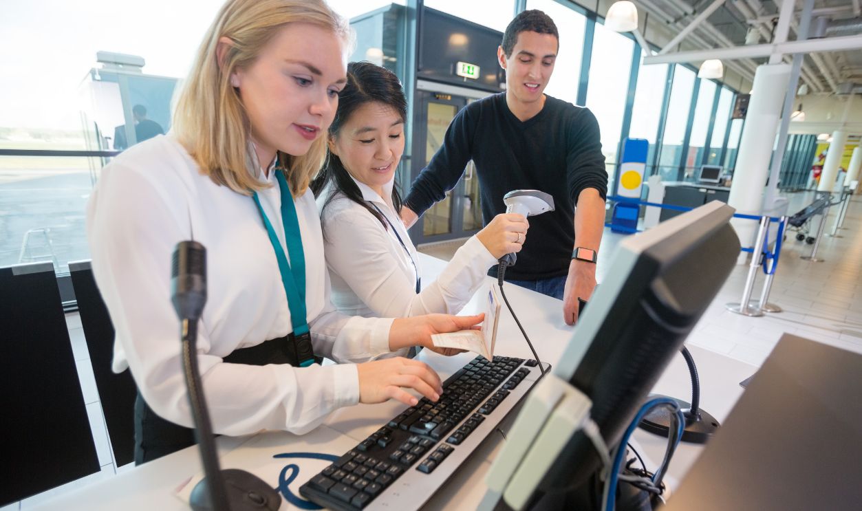 Receptionist With Passport Using Computer While Colleague Scanning