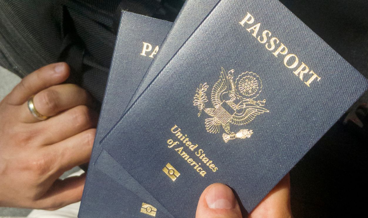 Male hand holding three U.S. passports in airport during check-in procedure