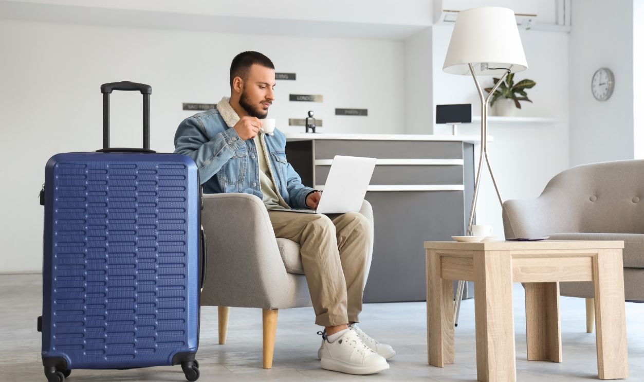 Shutterstock - 2770923057 - Young man with coffee and laptop waiting for his flight in airport lounge.