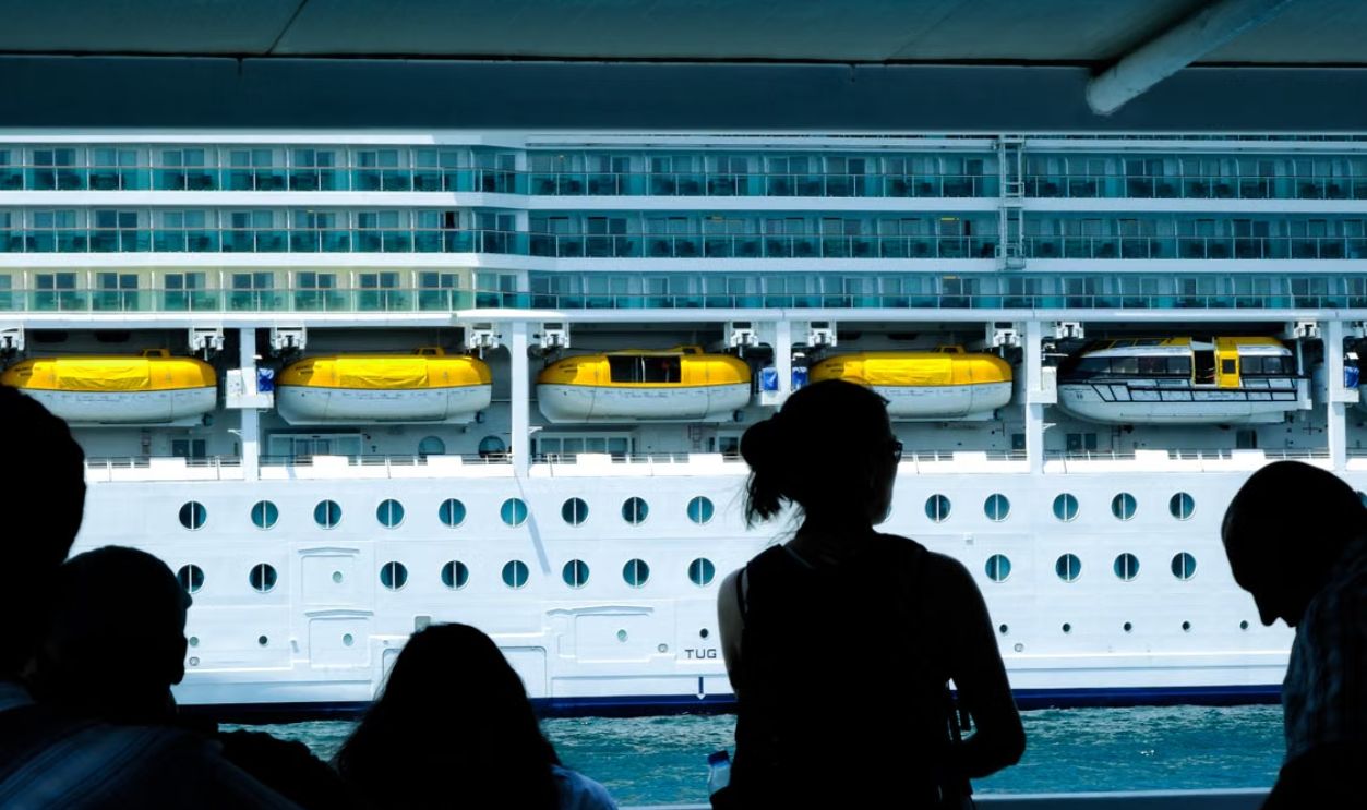 Silhouettes of people observing a large cruise ship from a dock in Turkiye.