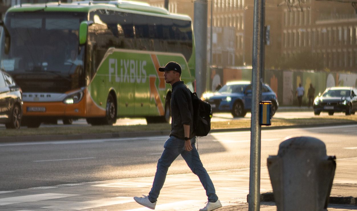 A man with a backpack walks across a bustling city street in the evening light.