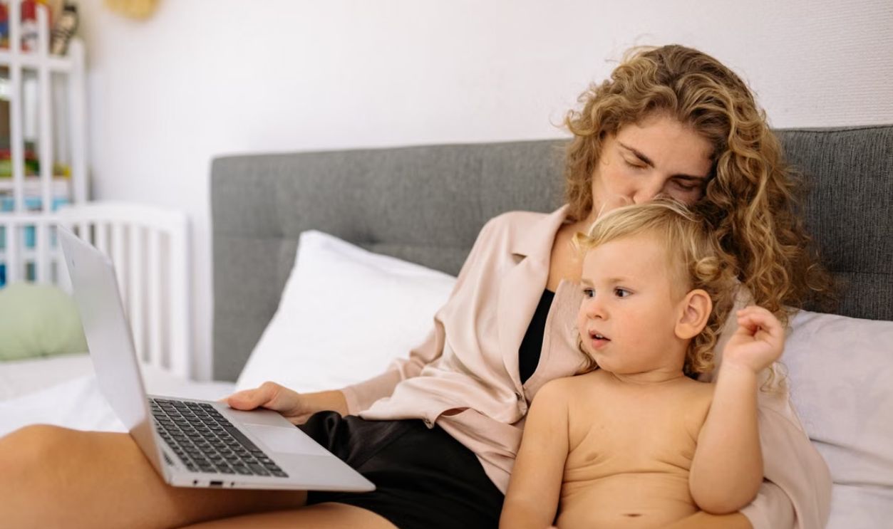 A mother and child relaxing together in bed, using a laptop. Family bonding indoors.