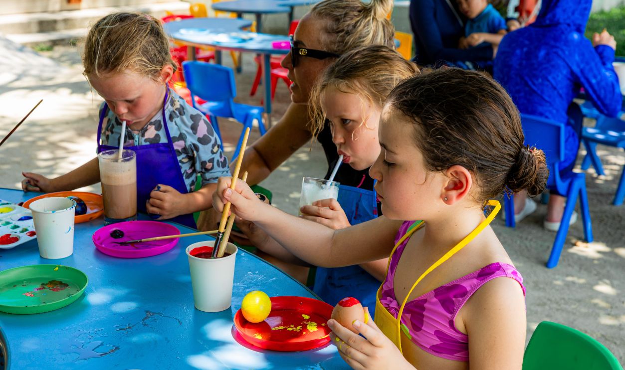 Children painting at an outdoor event while sipping refreshing beverages. Creative and joyful atmosphere.