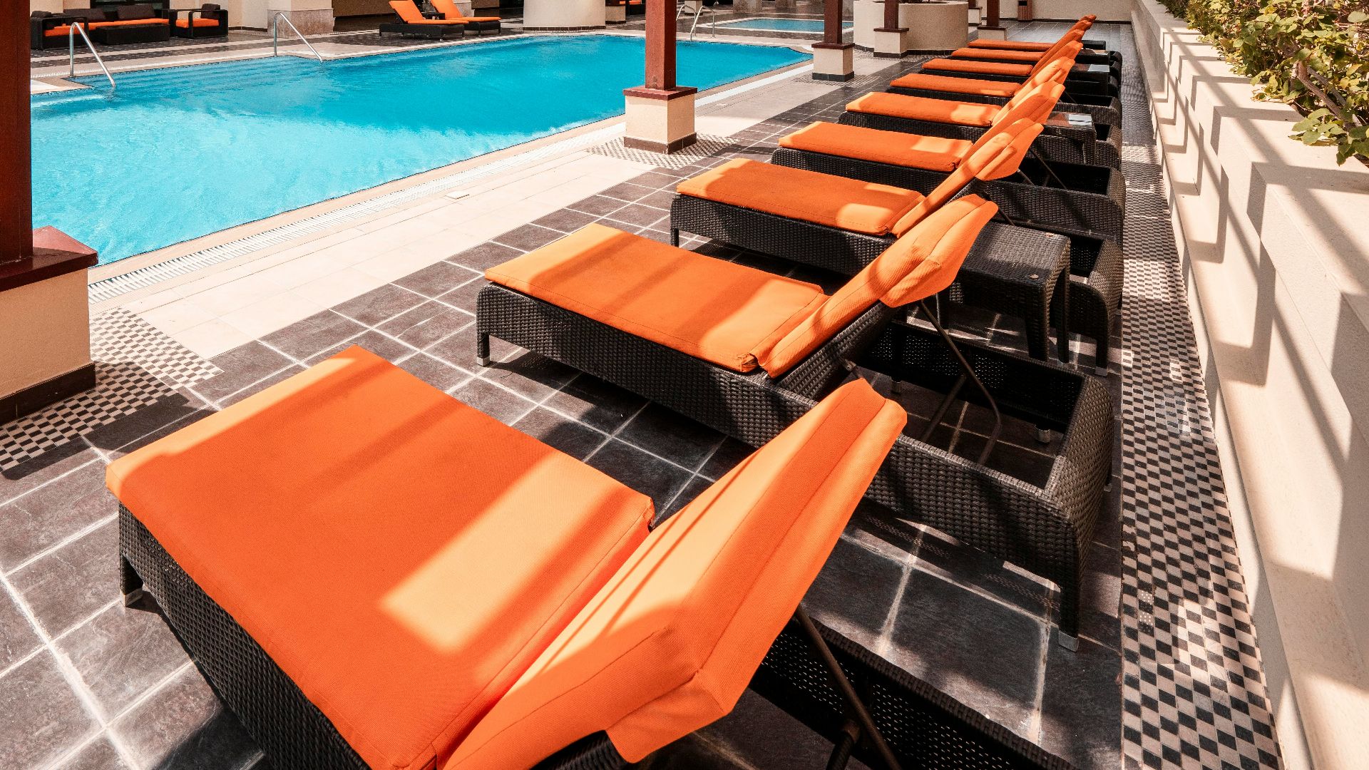 A long row of orange lounge chairs next to a swimming pool