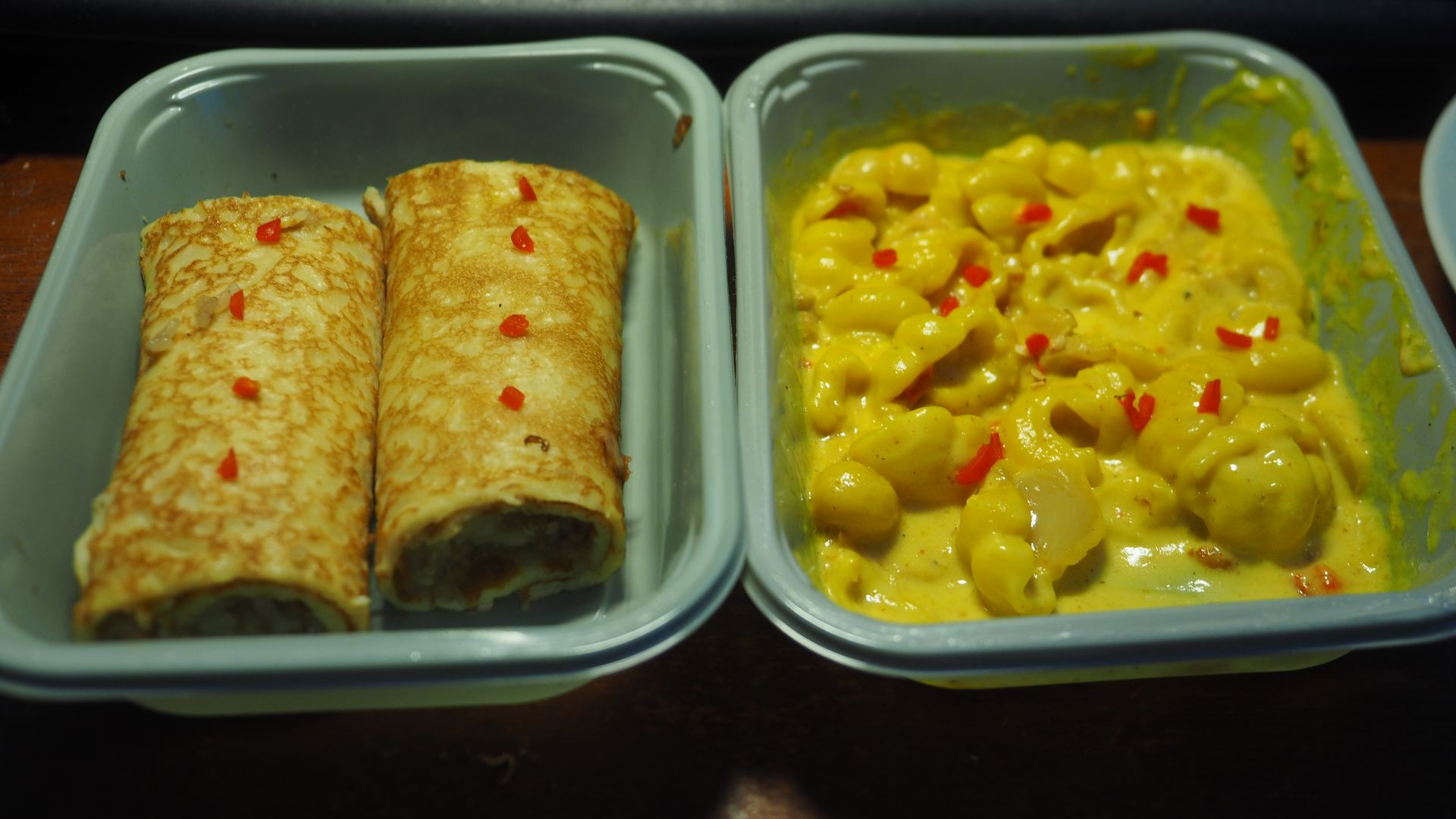 Two plates of convenience foods bought from a grocery store and eaten for lunch at a private apartment in Helsinki, Finland in July 2025. On the left is meat-filled crêpes, on the right is mac&cheese. Both have been sprinkled with very tiny bits of habane