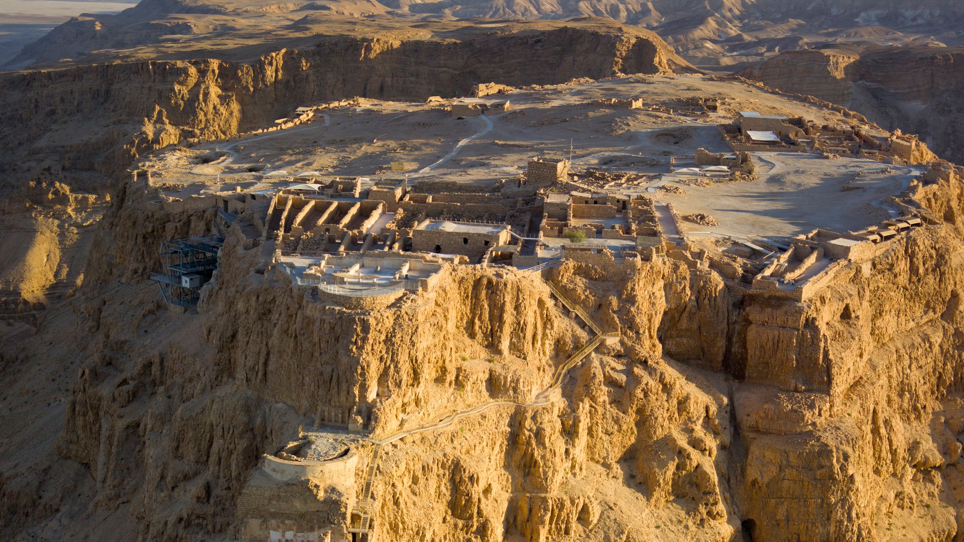 Aerial view of Masada (Hebrew מצדה), in the Judaean Desert (Hebrew: מִדְבַּר יְהוּדָה‎, Arabic: صحراء يهودا), with the Dead Sea in the distance.