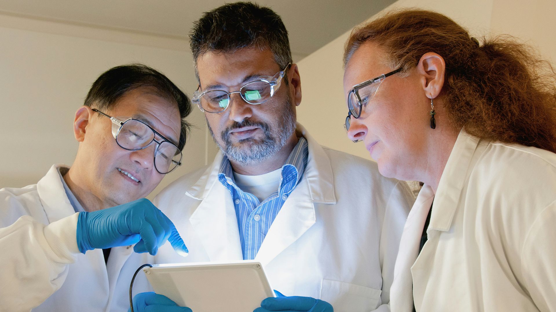 three people in lab coats looking at a tablet