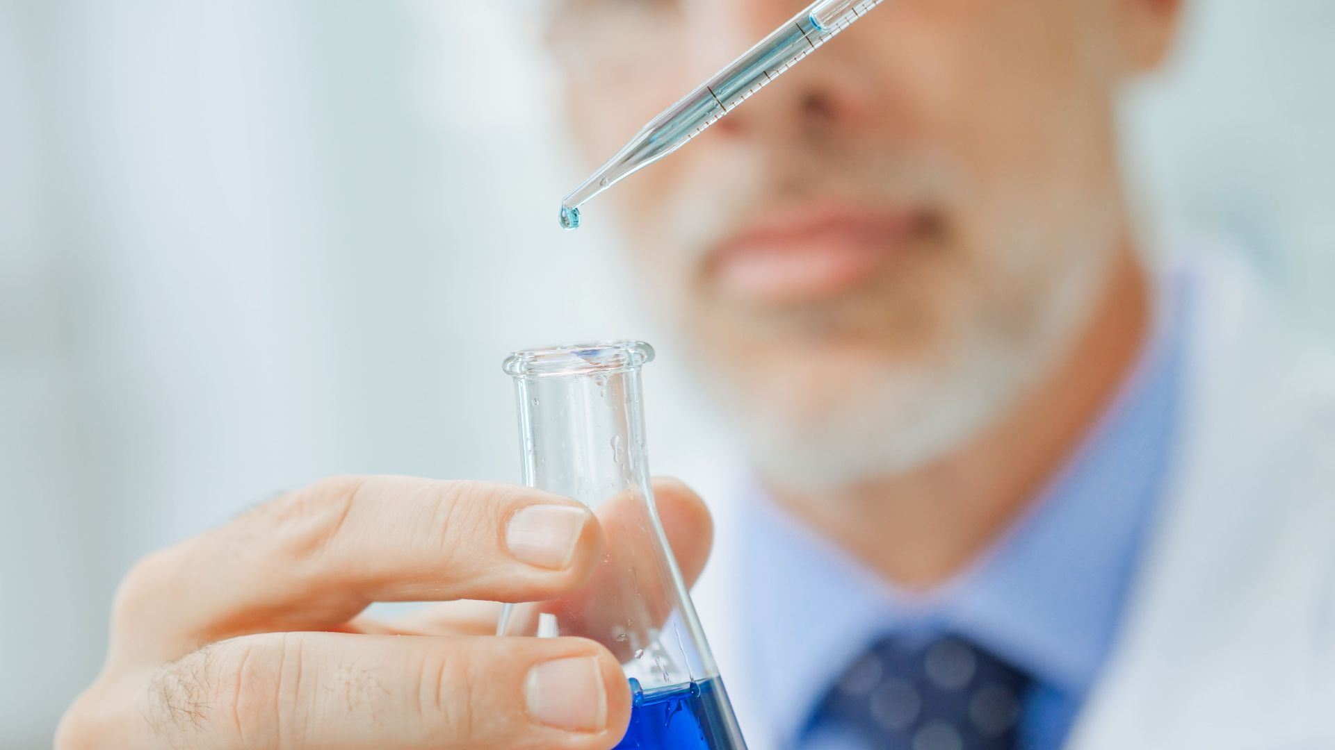 Scientist using pipette to drop liquid into Erlenmeyer flask in laboratory setting.