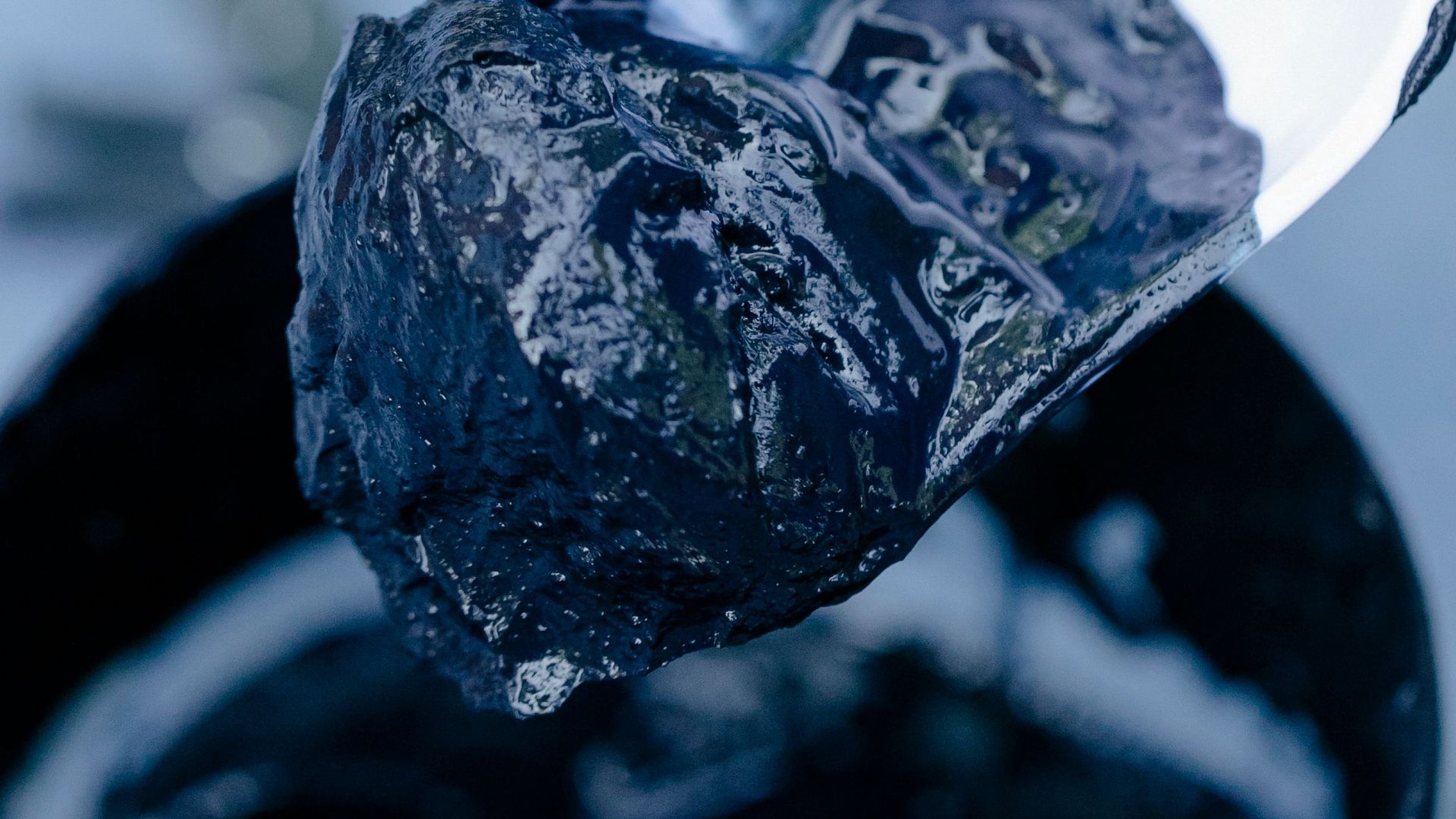 A detailed view of a hand with a spatula scooping dark mud from a jar, highlighting texture.