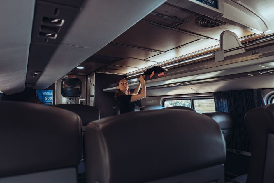 Female traveler stowing luggage in a train overhead compartment, emphasizing modern passenger travel.
