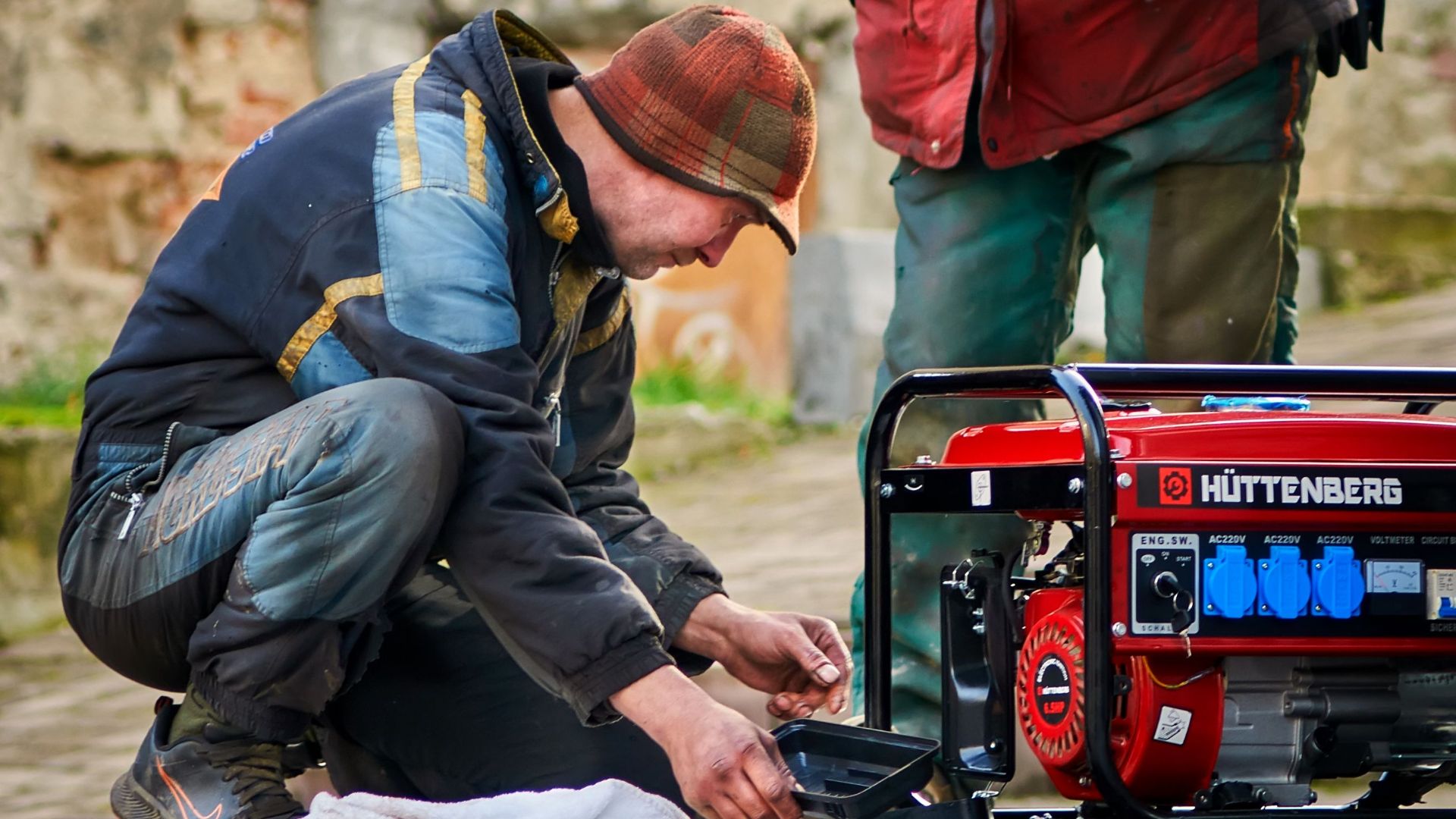 Two technicians working on a red HÜTTENBERG power generator outdoors.