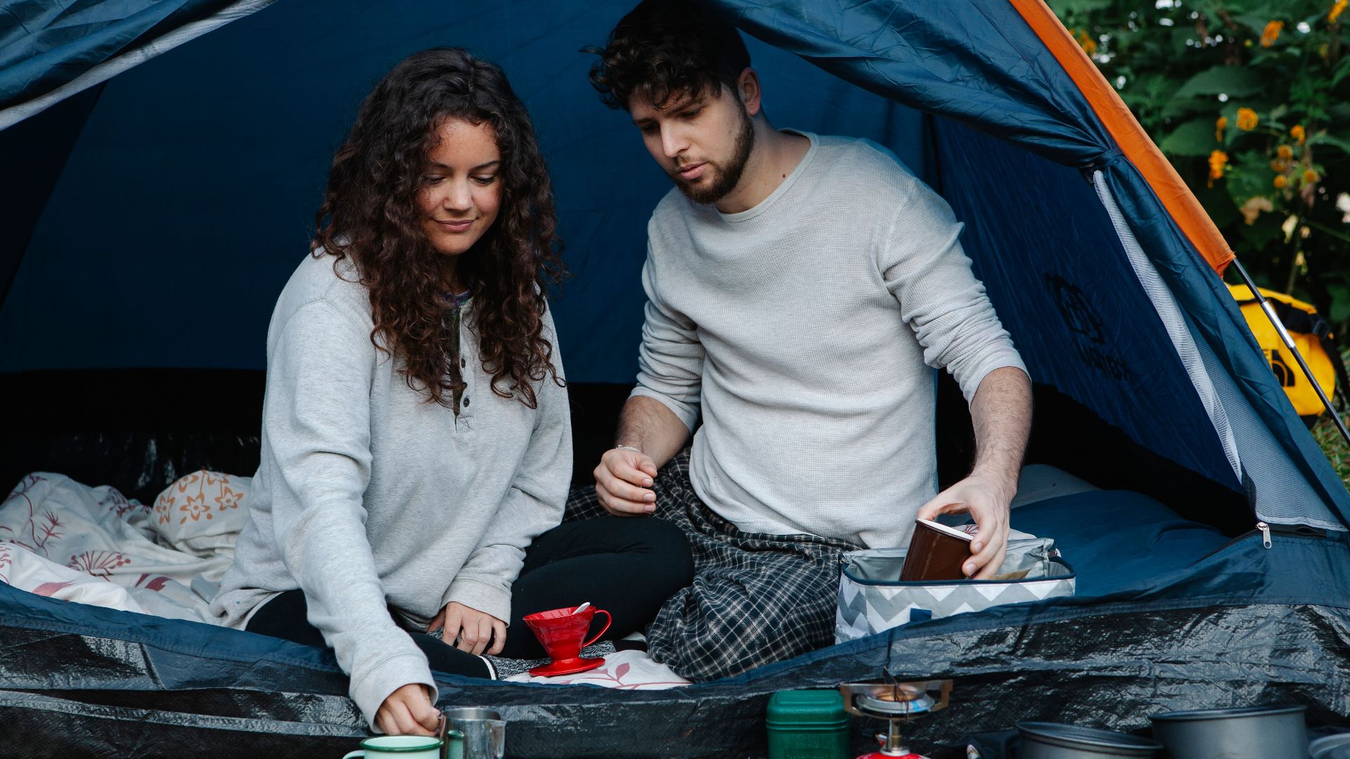 Young smiling couple in pyjamas making breakfast sitting in tent while spending holidays together in countryside