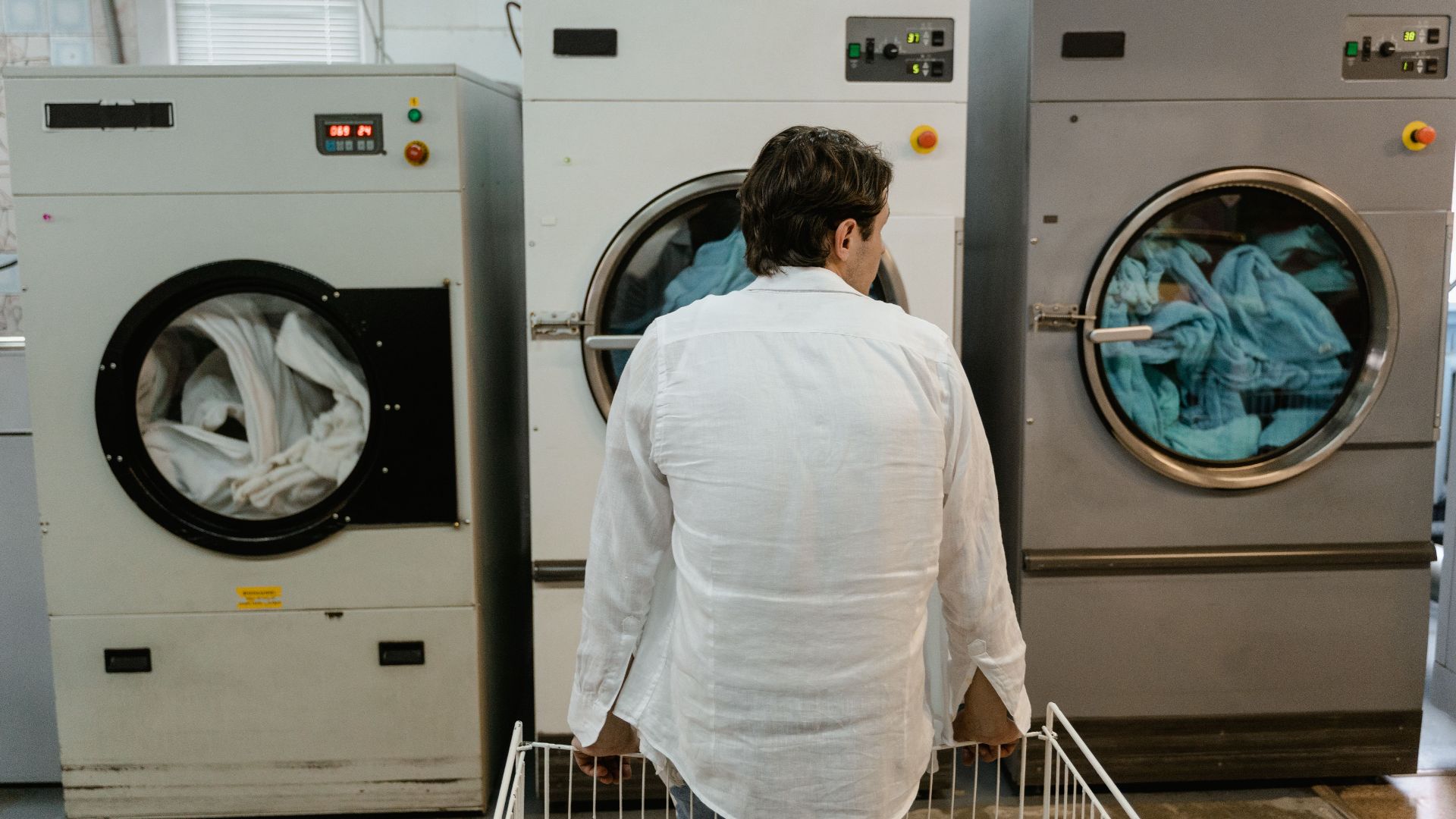 A man uses commercial washing machines at an indoor laundromat.