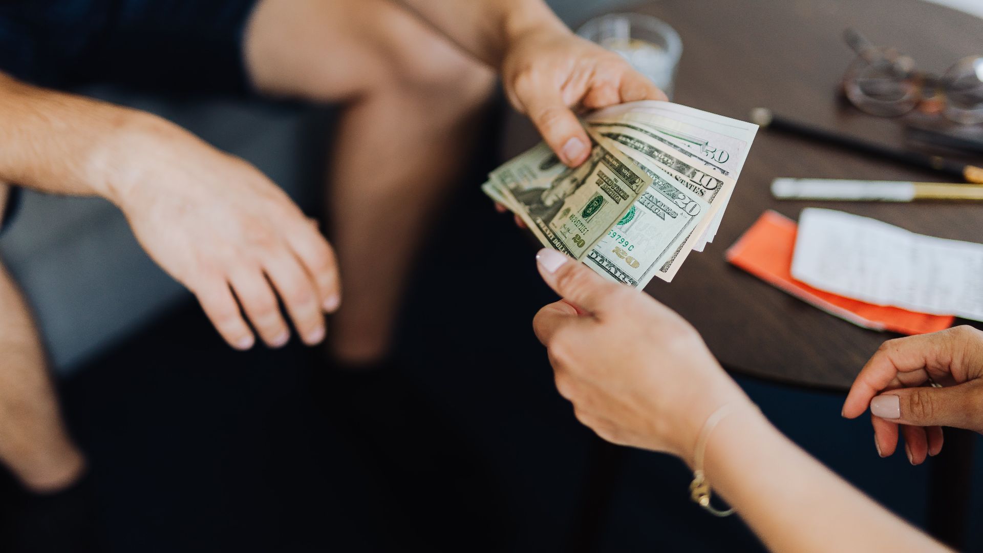 Close-up of hands exchanging US dollar bills, symbolizing a financial transaction or payment.