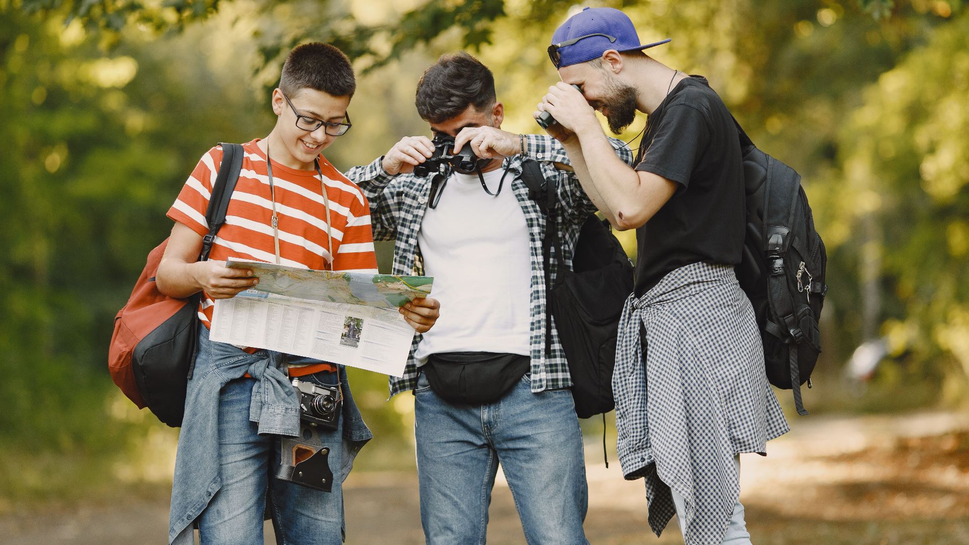 Three young men hiking and exploring a forest, using a map and binoculars.