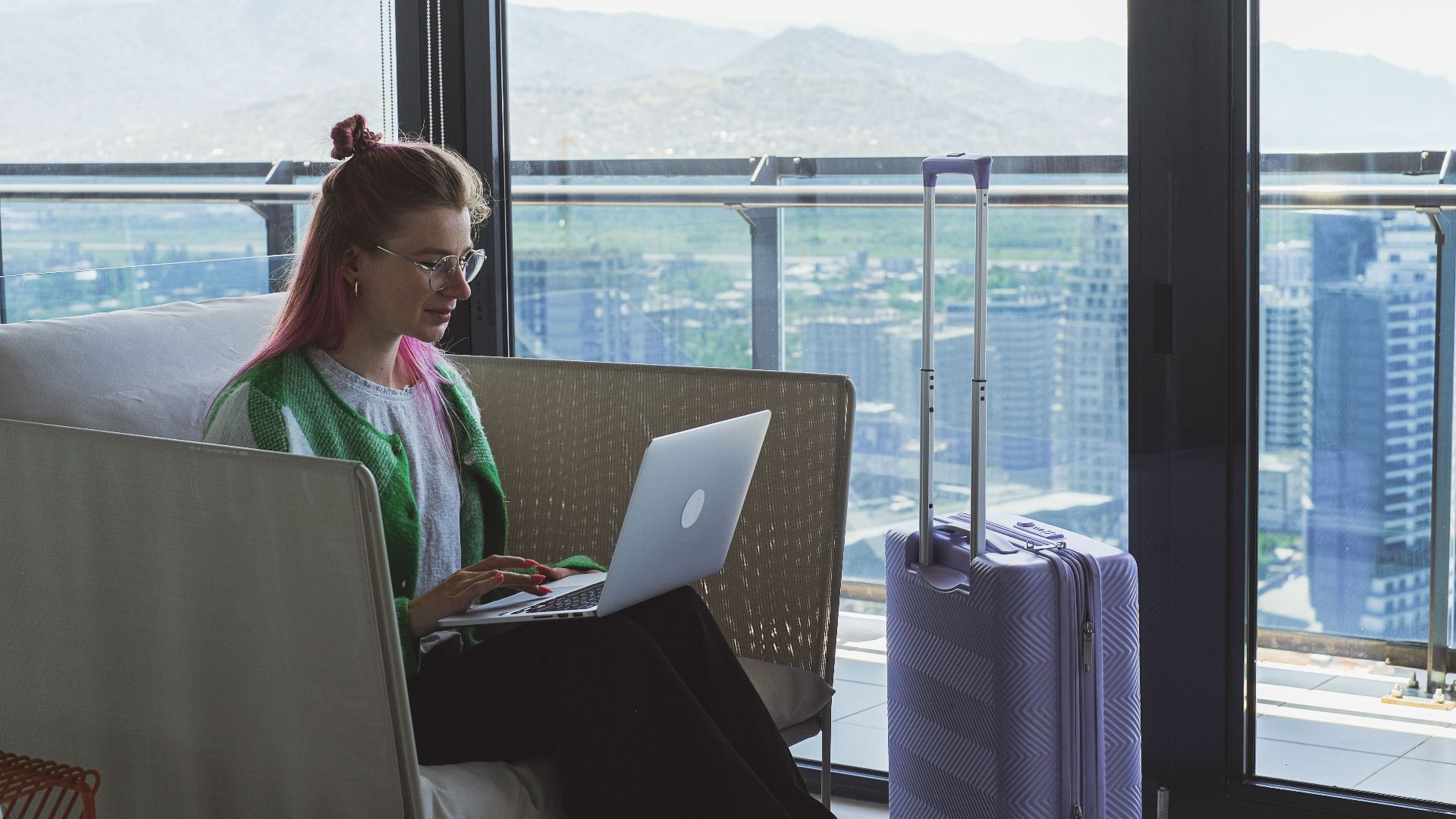 Woman working on a laptop in a hotel lounge with a stunning city view.